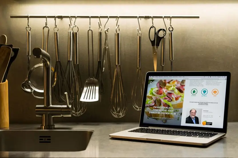 Bild zeigt eine Küchenzeile auf der ein Laptop steht, auf dem gerade die SJS-Catering-Website geöffnet ist.